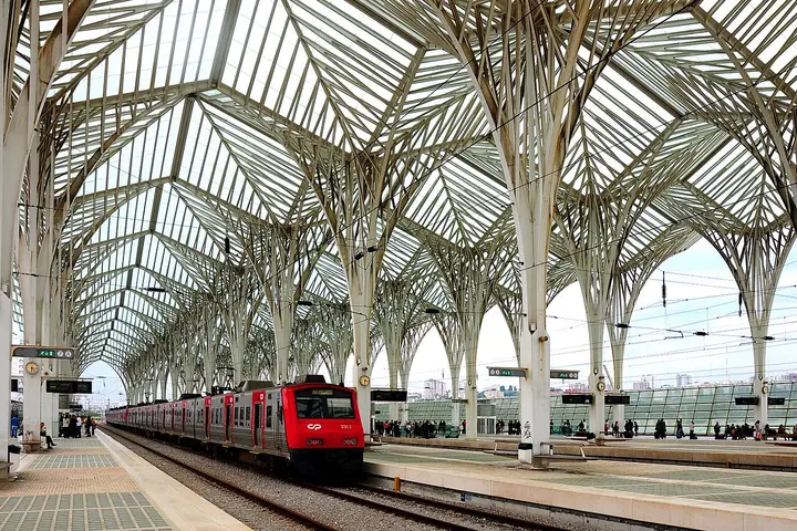 Cobertura em estrutura branca da Gare do Oriente sobre as linhas, com um comboio vermelho